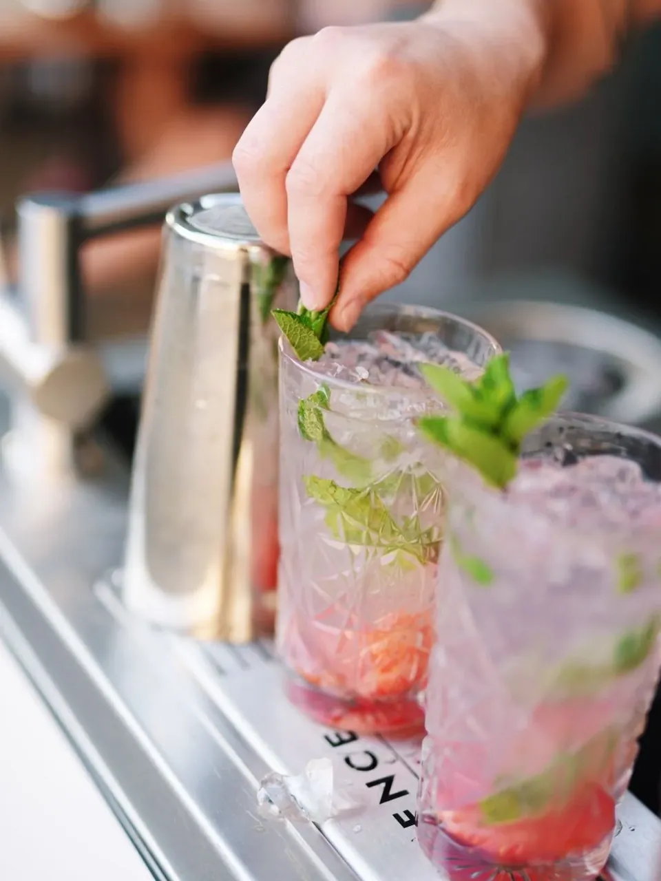 Een hand legt een muntsprietje op een getapte cocktail