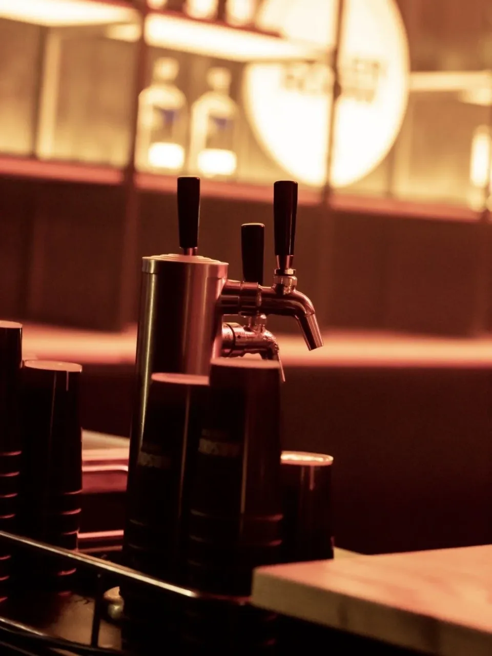 Een cocktailtapzuil met drie kranen op een bar, warm verlicht