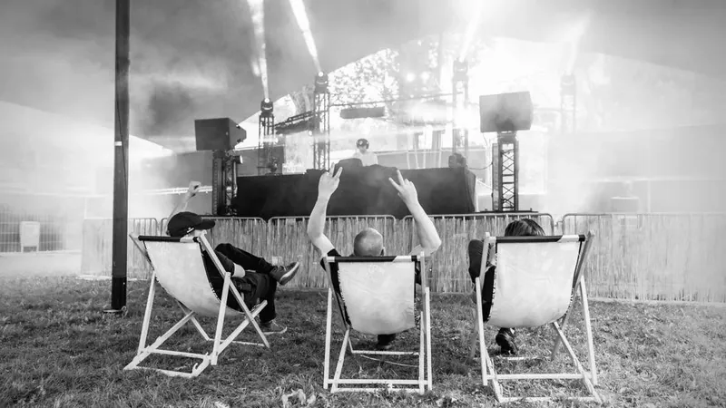 Drie vrienden in strandstoelen voor een festivalpodium, in zwart-wit